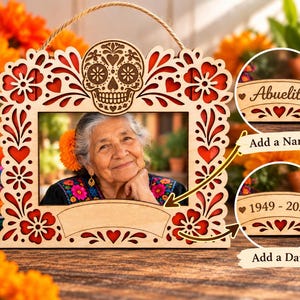 May include: A rectangular wooden picture frame featuring intricate laser-cut floral patterns and a central sugar skull design at the top. The frame includes a blank banner for personalization and a jute twine hanger for display purposes.