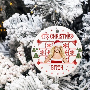May include: White ceramic Christmas ornament with a red and white pixelated design featuring a Christmas tree, snowflakes, and the text "It's Christmas Bitch". A photo of a woman wearing a Santa hat is in the center of the ornament.