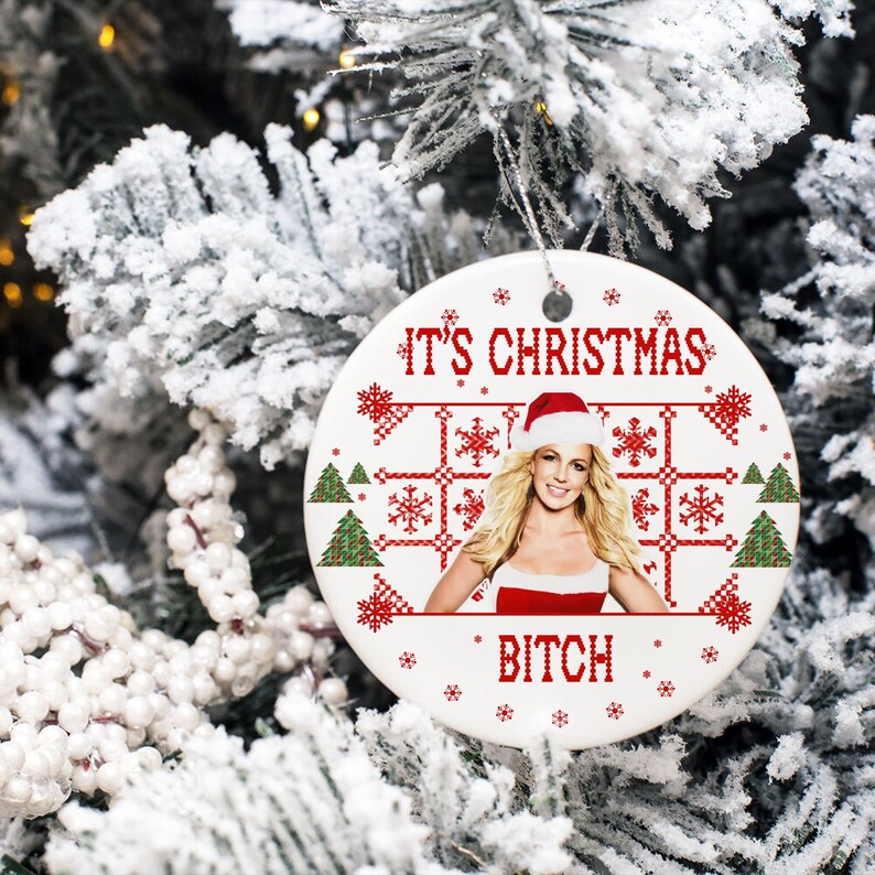 May include: White ceramic Christmas ornament with a red and white pixelated design featuring a Christmas tree, snowflakes, and the text "It's Christmas Bitch". A photo of a woman wearing a Santa hat is in the center of the ornament.