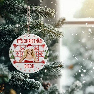 May include: White ceramic Christmas ornament with a red and white knitted pattern. The ornament features a photo of a woman wearing a Santa hat and a red dress. The text "It's Christmas Bitch" is printed on the ornament.