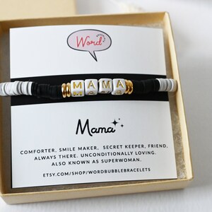 May include: A bracelet with black, white, and gold beads spelling "MAMA". The bracelet is presented in a gift box with a card that says "Mama" and lists positive attributes.