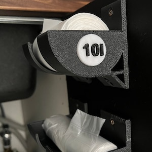 Könnte beinhalten: Zwei schwarze, wandmontierte Organizer aus Kunststoff zum Aufbewahren von Plastiktüten. Der obere Organizer hat ein weißes Etikett mit der Nummer "101" darauf. Der untere Organizer hat ein weißes Etikett mit der Nummer "251" darauf.
