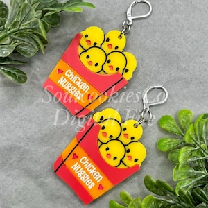 May include: A pair of earrings shaped like red and orange boxes with the text "Chicken Nuggets" and yellow chicken nuggets inside.