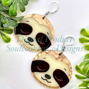May include: A pair of earrings featuring a sloth design. The earrings are made of resin and have a brown and white marbled pattern. The sloth has brown eyes and a brown nose. The earrings are attached to silver hooks.