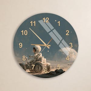 May include: A round wall clock featuring a dark blue space-themed background with an astronaut driving a lunar rover on a cratered surface. The clock face displays gold-colored numbers from 1 to 12 and thin gold hands for the hour, minute, and second.