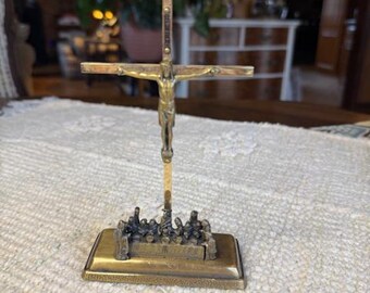 May include: A bronze crucifix with a detailed depiction of Jesus on the cross. The base features a relief of figures. The cross is mounted on a rectangular base, and the overall design is ornate and detailed.