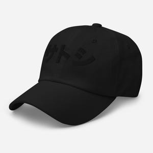Puede incluir: Una gorra de béisbol negra con la palabra japonesa "サトシ" bordada en negro en la parte delantera.