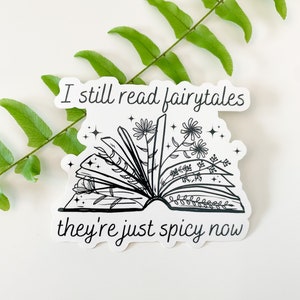 May include: Black and white sticker with an open book with flowers growing out of it. The text reads "I still read fairytales they're just spicy now".