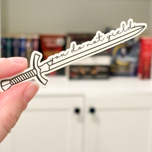 May include: A white sticker with a black outline of a sword. The sword has the text "you do not yield" written on it.