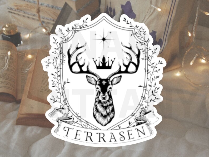 May include: Black and white illustration of a deer head with antlers inside a shield-shaped frame with a crown and the word "TERRASEN" at the bottom. The frame is surrounded by leafy branches.
