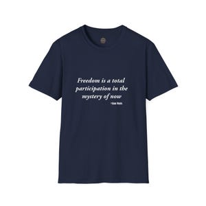 May include: Navy blue t-shirt with the quote "Freedom is a total participation in the mystery of now" by Alan Watts printed in white. The shirt has a crew neck and short sleeves, perfect for casual wear.