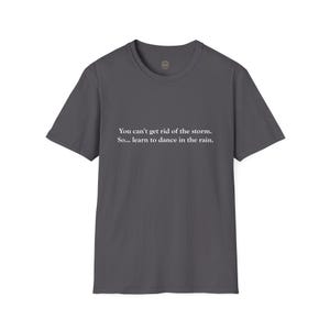 May include: Dark gray t-shirt with the text "You can't get rid of the storm. So... learn to dance in the rain." The shirt has short sleeves and a crew neck. The text is in a simple, white font.