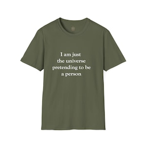 May include: Olive green t-shirt with the text "I am just the universe pretending to be a person" in white. The shirt has a crew neck and short sleeves. The fabric appears to be a soft cotton blend.