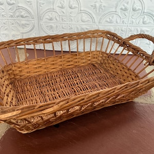 May include: A woven wicker basket with a handle. The basket is rectangular and has a light brown color.