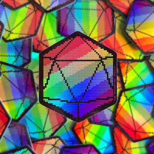 May include: A collection of holographic stickers featuring a rainbow-colored, geometric design. The stickers have a black outline and a pixelated appearance, resembling a D20 die. The stickers are scattered across a surface.