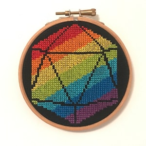 Op de afbeelding: Een regenboogkleurig kruissteekontwerp van een 20-zijdige dobbelsteen, of d20, in een houten borduurring.