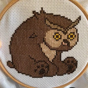 May include: A brown and beige cross-stitch embroidery of an owl with yellow eyes, framed in a wooden hoop.