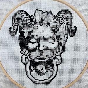 Może przedstawiać: Czarno-białe haftowane krzyżykiem przedstawiające stworzenie z rogami, brodą i pierścieniem w pysku.