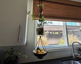 May include: A black macrame plant hanger with two potted plants and a bowl of lemons hanging from the ceiling in a kitchen.