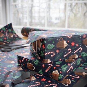 Puede incluir: Dos cajas de regalo envueltas en papel azul marino con un patrón festivo de bastones de caramelo, tazas de café, estrellas y vegetación. Un rollo de papel de regalo a juego y unas tijeras son visibles. Cinta negra en primer plano.