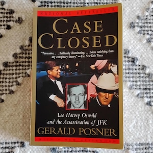 May include: A book titled "Case Closed: Lee Harvey Oswald and the Assassination of JFK" by Gerald Posner. The cover features a black and white photo of Lee Harvey Oswald, a color photo of President John F. Kennedy, and a color photo of a man in a hat.