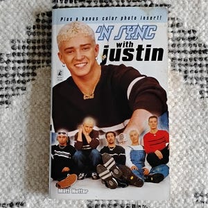 May include: A book cover featuring a photo of a boy band, 'N Sync, with the text 'N Sync with Justin' on the cover. The band members are wearing casual clothing and are posing for a photo.