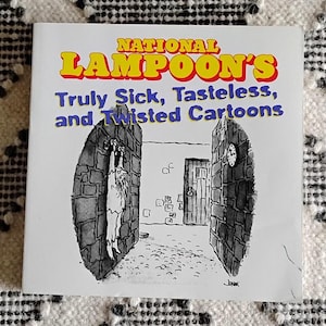 May include: A National Lampoon's book cover with the title in yellow and red, and the subtitle in blue. The cover features a black and white cartoon of a person hanging from a stone wall.