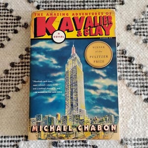May include: A hardcover book titled "The Amazing Adventures of Kavalier & Clay" by Michael Chabon. The cover features a cityscape with the Empire State Building and a yellow and red title. It is a Pulitzer Prize winner.
