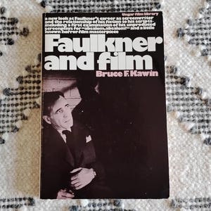 May include: A book titled "Faulkner and Film" by Bruce F. Kawin. The cover features a black background with white text and a photo of a man in a suit. The book is part of the Ungar Film Library series.