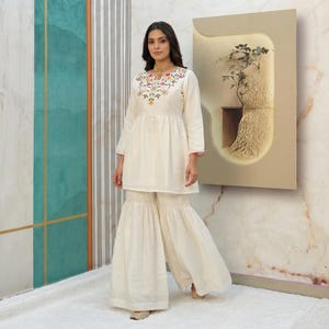 Può includere: Completo tunica e pantaloni palazzo ricamati bianco sporco. La tunica presenta uno scollo tondo con ricami floreali colorati e maniche a tre quarti. I pantaloni palazzo hanno una gamba ampia e svasata. L'outfit è realizzato in tessuto leggero.