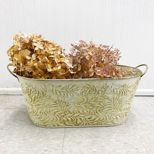Peut inclure: Un pot en métal blanc avec un motif en relief floral. Le pot a deux poignées et est rempli d'hortensias séchés.