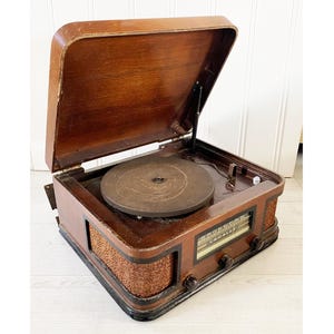 May include: A vintage Crosley record player with a wooden cabinet and a hinged lid. The record player has a dark brown finish, a round turntable, and a radio dial. The sides of the cabinet have a woven texture.
