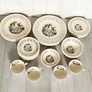 Peut inclure: Service de table vintage crème. L'ensemble comprend des assiettes, des bols et des tasses avec une bordure dorée et une illustration détaillée d'un couple et d'un musicien. Chaque pièce présente une scène romantique.