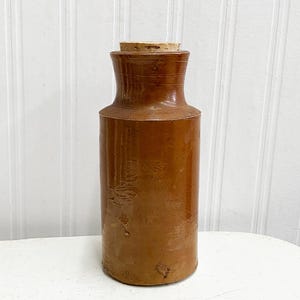 May include: A brown ceramic bottle with a cork stopper. The bottle has a rounded bottom and a slightly flared neck.
