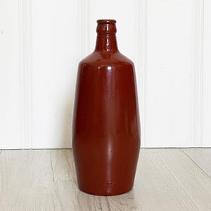 May include: A terracotta colored ceramic bottle with a rounded body and a narrow neck.
