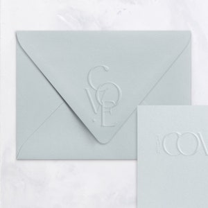 May include: A light blue envelope with a raised, embossed design of the word "LOVE" in a stylized font. The envelope is lying flat on a white surface.
