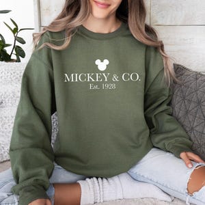 a woman sitting on a couch wearing a mickey and co sweatshirt