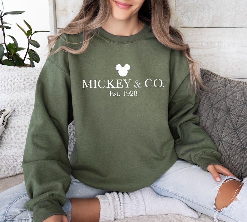a woman sitting on a couch wearing a mickey and co sweatshirt