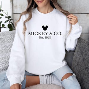 a woman sitting on a couch wearing a mickey and co sweatshirt