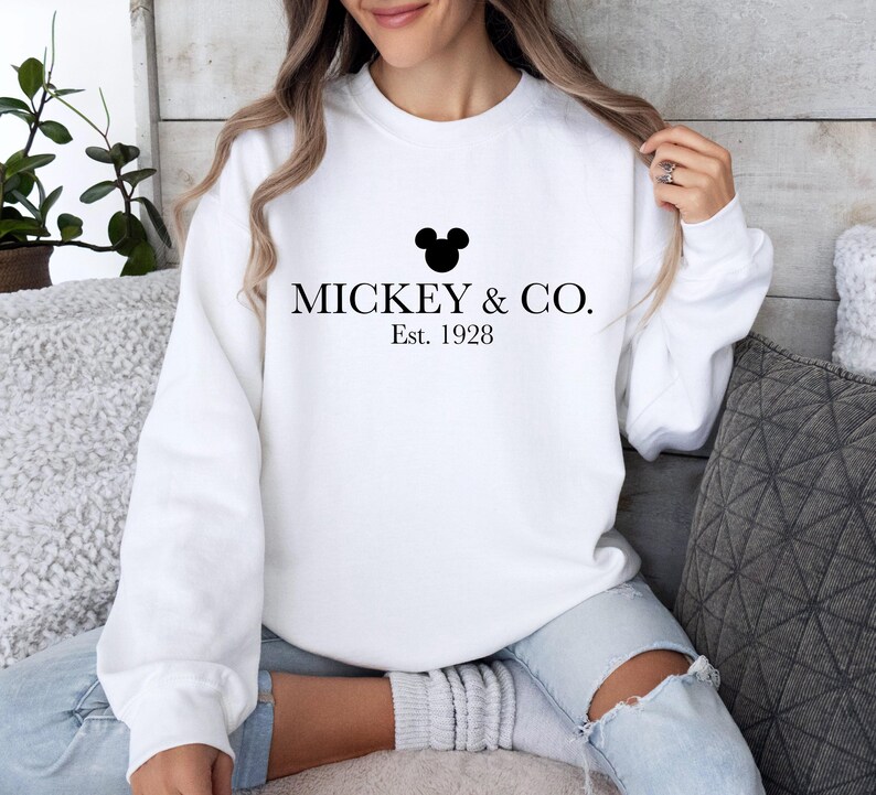 a woman sitting on a couch wearing a mickey and co sweatshirt