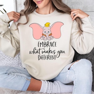 a woman sitting on a couch wearing a sweatshirt that says embrace what makes you different