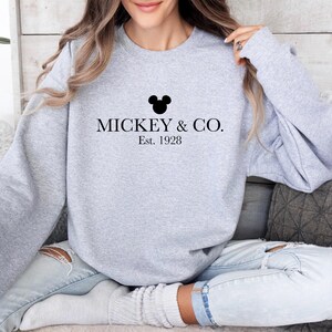 a woman sitting on a couch wearing a mickey and co sweatshirt