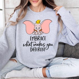 a woman sitting on a couch wearing a sweatshirt that says embrace what makes you different