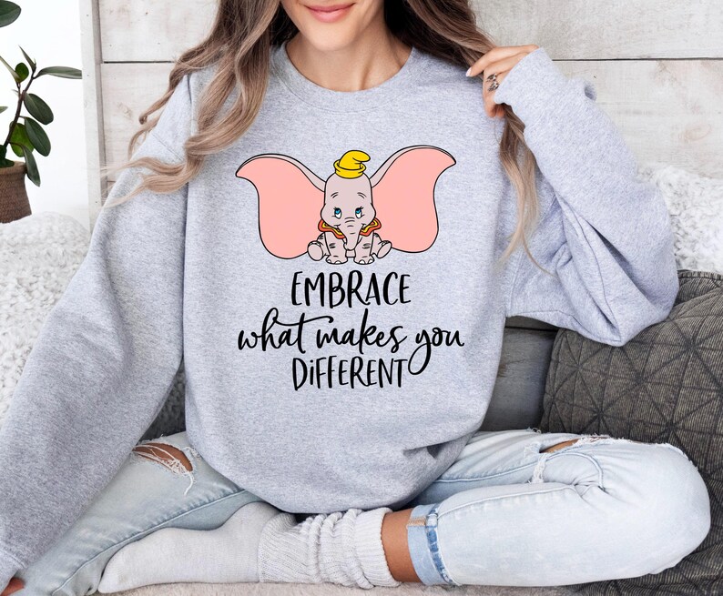 a woman sitting on a couch wearing a sweatshirt that says embrace what makes you different