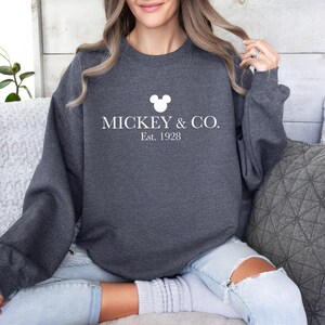 a woman sitting on a couch wearing a mickey and co sweatshirt