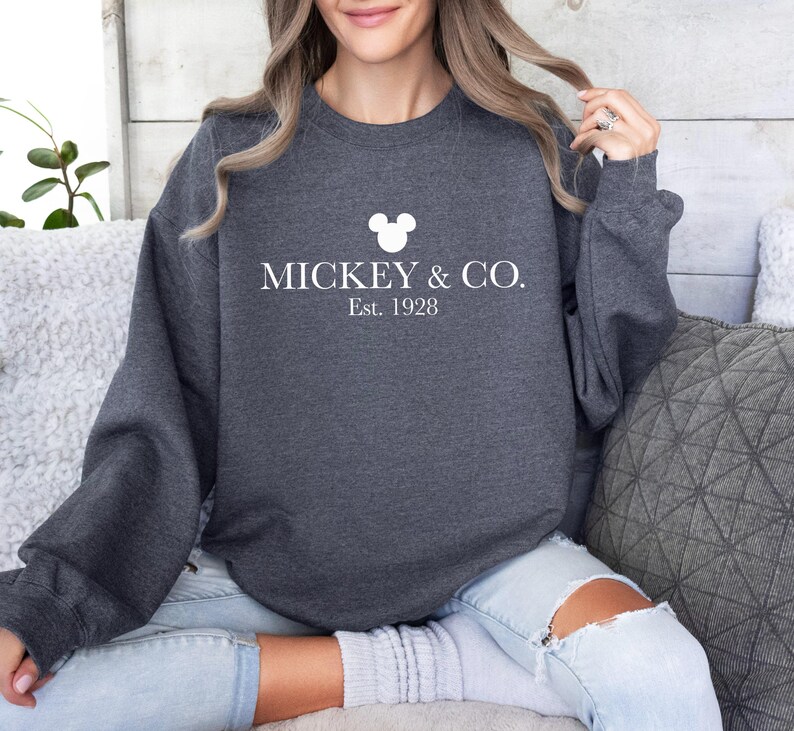 a woman sitting on a couch wearing a mickey and co sweatshirt