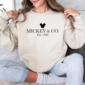 a woman sitting on a couch wearing a mickey and co sweatshirt