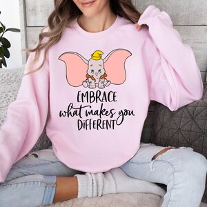 a woman sitting on a couch wearing a pink sweatshirt