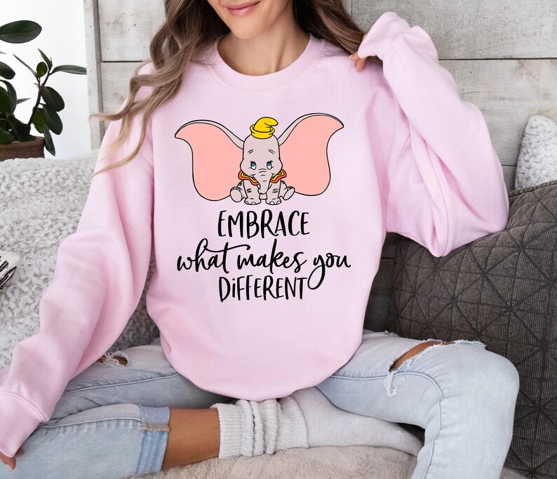 a woman sitting on a couch wearing a pink sweatshirt
