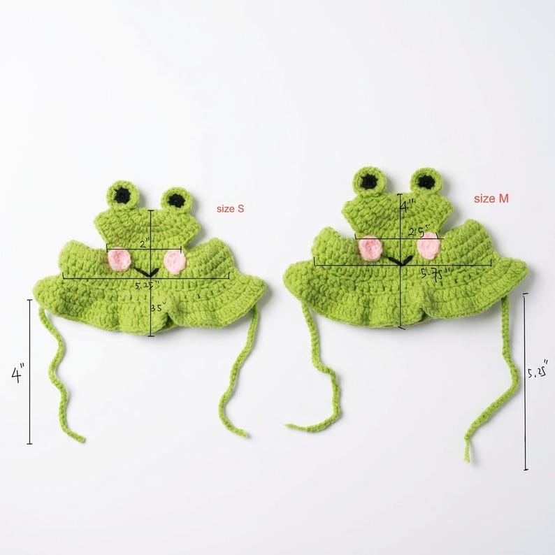 May include: Two green crochet frog hats with pink cheeks and black eyes. The size S hat measures 2 inches wide at the top, 5.25 inches wide at the base, 3.5 inches tall, and has 4-inch ties. The size M hat measures 4 inches wide, 5.75 inches wide, 4 inches tall, and has 5.25-inch ties.